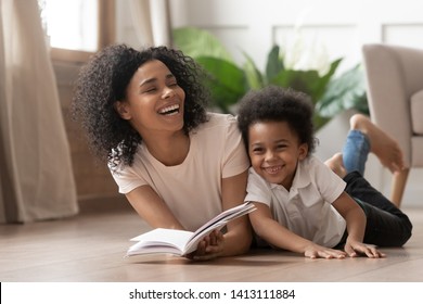 Caring african american mother baby sitter tell funny fairy tale story to smart cute kid son laugh lay on warm floor together, loving mixed race mom read book having fun with little child boy at home