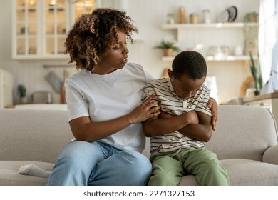 Caring African American mother calms offended child boy while sitting on couch after quarrel at home. Attentive Mom hugs support upset schoolboy with pout lips and crossed hands due to school failures - Powered by Shutterstock