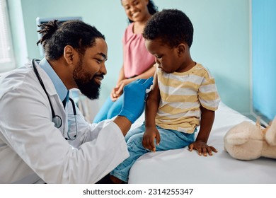 Caring African American pediatrician preparing arm of a small boy for vaccination at doctor's office. - Shutterstock ID 2314255347