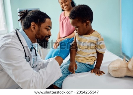 Caring African American pediatrician preparing arm of a small boy for vaccination at doctor's office.