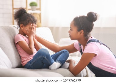 Caring african american teen girl calming her sad crying baby sister, side view