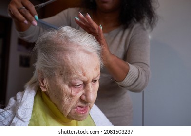 Caring African American Woman Caregiver, Cutting Her Elderly Woman Hair At Home
