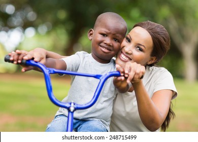 Caring African American Woman Helping Her Son To Ride A Bike In Park