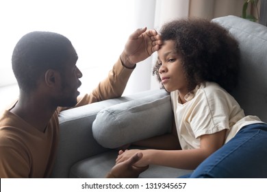 Caring African Father Touching Forehead Of Sick Ill Kid Daughter Lying On Couch, Worried Black Dad Checking Child Temperature, Fever Flu Symptoms And Treatment, Children Medical Health Care Concept