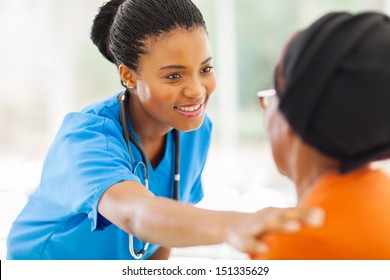 caring african medical nurse comforting senior patient in office