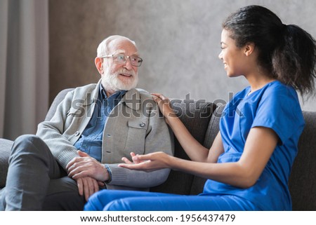 Caring african-american nurse talks to old elderly senior patient holds his hand sit in living room at homecare visit provide psychological support listen complains showing empathy encouraging.
