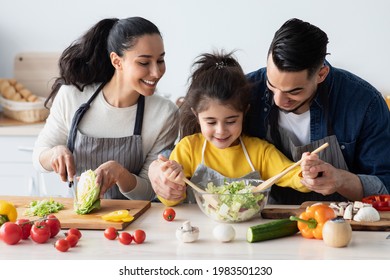 Caring Arab Parents Cooking With Their Little Daughter In Kitchen Together, Modern Muslim Family Of Three Having Fun At Home While Preparing Food, Father Showing Child How To Make Salad, Closeup - Powered by Shutterstock