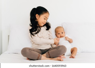 Caring Asian girl in casual wear with crossed legs holding hand of small brother sitting on bed in house - Powered by Shutterstock