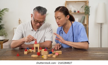 Caring Asian Woman Care Attendant Giving Instructions While Assisting Elderly Patient Go Through Rehab Treatment For Parkinson’s Disease With Building Blocks At Home