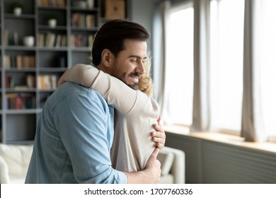 Caring attentive grown up son visited mother, older mom hugs adult millennial child she missed him enjoy moment, relatives people standing inside of cozy living room feels happy, family bonds concept