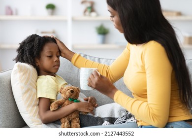 Caring Black Mother Giving Hot Tea To Her Ill Little Daughter And Touching Her Forehead, Loving African American Mom Taking Care About Sick Female Child Suffering Seasonal Flu Or Cold, Closeup - Shutterstock ID 2127443552