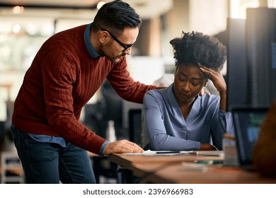 Caring businessman consoling his distraught African American female colleague while she's working on desktop PC in the office. - Powered by Shutterstock