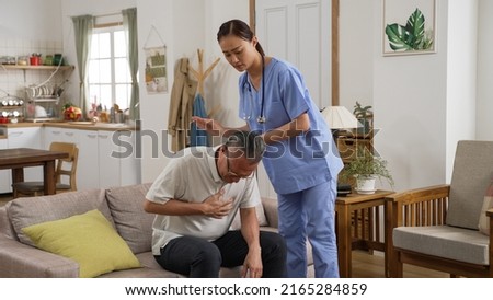 caring chinese nursing aide patting on elderly male patient’s back to help clear sputum from lung during home visit. she takes a pause and asks if he is ok while he is coughing hard
