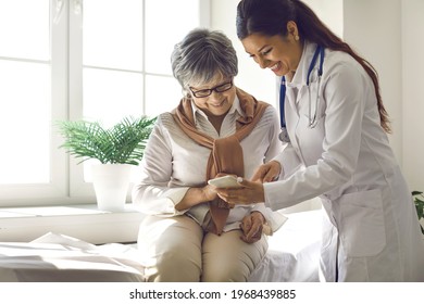 Caring Doctor Teaches Female Patient To Use Mobile Healthcare App. Retired Lady Sitting In Hospital Exam Room Looking At Cell Screen Learning To Download Health Tracker For Senior Citizens. Copy Space