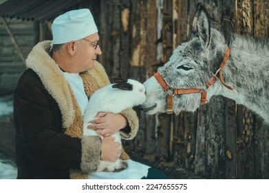Caring doctor veterinarian holds a rabbit in his arms and a donkey next to him. The veterinarian examines the animals - Powered by Shutterstock