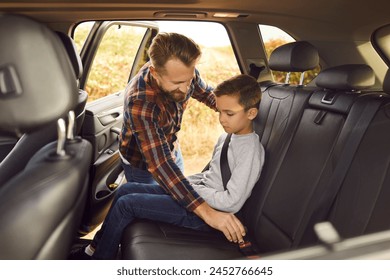 Caring father is buckling up seat belt for his young son in back seat of family car. Man helps child fasten seat belt in car before traveling together. Concept of parental safety and responsibility. - Powered by Shutterstock