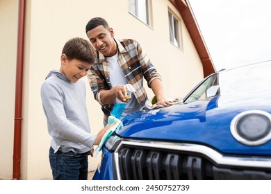 Caring father cleaning automobile with his son together, boy wiping while dad washing car with rag and spray - Powered by Shutterstock