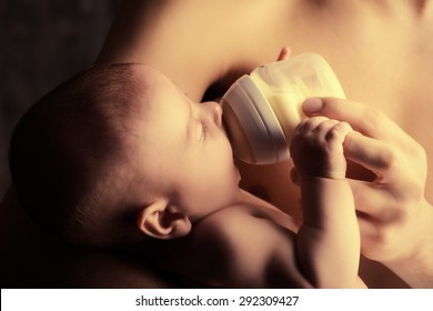 Caring Father Feeding His Baby From A Bottle. Healthy Baby Food And Infant Formula, Milk. Studio Shot Over Black Background.