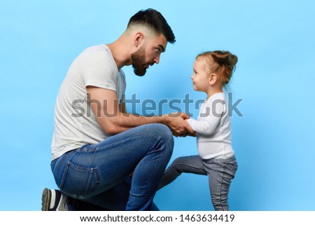caring father and little obedient daughter who listens to the instruction of parent on blue isolated background. daddy making an observation to kid. dad asking daughter to behave well