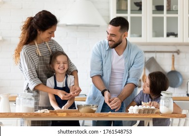 Caring father and mother playfully teaching little children to cooking pastry standing at table in kitchen. Happy smiling dad and mom with son and daughter playing with flour preparing dinner. - Shutterstock ID 1761548753