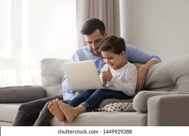 Caring Father Teaching Adorable Little Son To Use Laptop, Dad And Preschool Boy Child Looking Computer Screen, Playing Game, Watching Video Or Cartoons, Sitting On Couch Together, Family Weekend