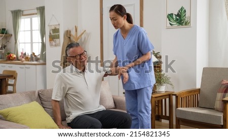 Caring female Asian personal nursing aide helping senior stroke patient do rehabilitation training in the living room at home. she lifts his arm slowly