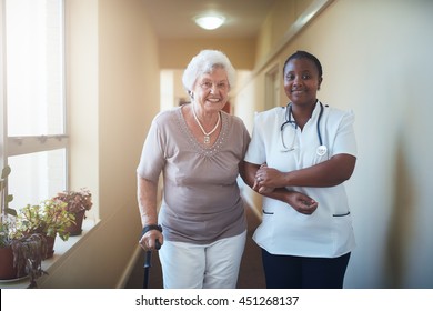 Caring Female Nurse Assisting A Senior Patient To Walk. Healthcare Worker And Senior Woman Together At Nursing Home