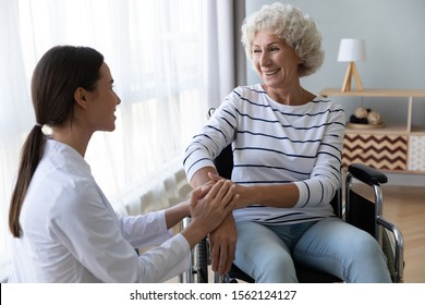 Caring Female Nurse Caregiver Hold Hand Support Disabled Elder Woman Patient Sit On Wheelchair At Home Hospital, Young Doctor Carer Help Paralyzed Old Granny On Wheel Chair, Senior Homecare Concept