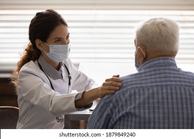 Caring Female Nurse In Medical Facemask Touch Calm Support Elderly Male Patient In Hospital. Supportive Woman Doctor In Facial Mask Show Empathy Comfort Mature Man In Clinic. Healthcare Concept.