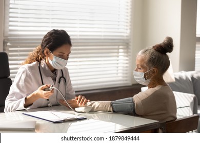 Caring Female Nurse In Medical Facial Mask Measure Check Blood Pressure Of Mature Woman Patient. Doctor Or GP Do Regular Checkup Examine Senior Client In Hospital. Elderly Healthcare Concept.