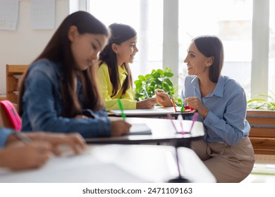 Caring female teacher providing assistance to schoolgirl, helping pupil during test, fostering an environment of support and focused learning, classroom interior - Powered by Shutterstock