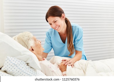 Caring Geriatric Nurse Cares For Ill Senior Citizen In Nursing Home Or Hospice