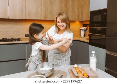 Caring grandmother and little granddaughter are having fun baking cookies together in the home kitchen. A loving elderly grandmother and granddaughter prepare a delicious sweet cake. - Shutterstock ID 2279199627