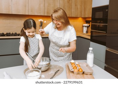 Caring grandmother and little granddaughter are having fun baking cookies together in the home kitchen. A loving elderly grandmother and granddaughter prepare a delicious sweet cake. - Shutterstock ID 2279199631