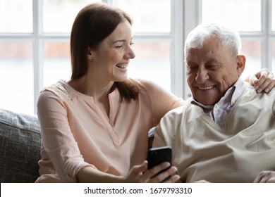 Caring grown up granddaughter and grandfather sit on couch holding cellphone. Young generation teach old how make videocall, to web surfing. Caretaker help to 80s man with virtual app services concept - Powered by Shutterstock