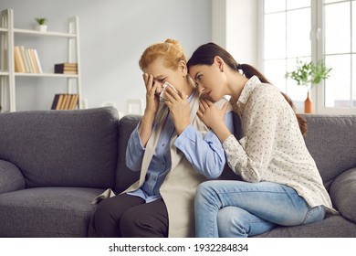 Caring Grown-up Daughter Comforting Her Senior Mother Who's Crying Sitting On Sofa At Home. Loss Of Family Member, Grief, Soothing, Support, Help And Care Concept