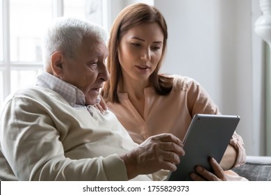 Caring Grownup Daughter Teaching Older Father To Use Computer Tablet Close Up, Pointing At Screen, Mature Man Asking Questions About Mobile Device To Young Woman, Elderly And Technology Concept