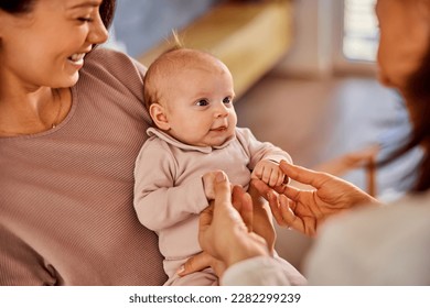 A caring happy mother holding her little baby girl in her arms during the female pediatrician's home visit examination. - Shutterstock ID 2282299239