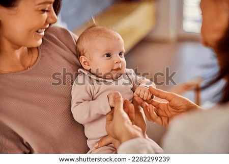 A caring happy mother holding her little baby girl in her arms during the female pediatrician's home visit examination.