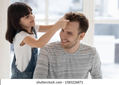 Caring happy preschool daughter brushing combing father hair. Help with hairstyle in morning, smiling little girl with sitting dad at home together playing with toy. - Shutterstock ID 1583226871