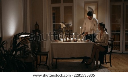 Caring husband pouring wine at romantic date zoom on. Young couple having anniversary dinner in evening home. Tender woman sitting guy serving table. Happy family at birthday celebration indoors