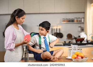 Caring Indian mother preparing kid for school by placing lunch box and water in bad - concept of responsibility, parental caring and back to school - Powered by Shutterstock