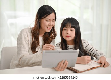 Caring and kind young Asian female sister teaching online lesson to her little sister, looking at tablet screen together. - Powered by Shutterstock