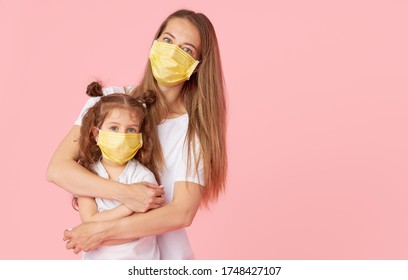 Caring for loved ones. Young mother hugs little daughter in protective medical masks during Covid-19 pandemics. Studio pink background - Powered by Shutterstock