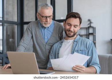 Caring loving adult son helping his old senior elderly father paying bills, counting money, doing paperwork at home together. Aid to elderly generation. Happy father`s day! - Powered by Shutterstock
