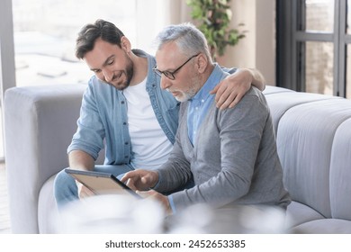 Caring loving adult son hugging embracing his old elderly senior father while he is showing his family photograph photo at home, telling stories of his youth. Happy father`s day! I love you, dad! - Powered by Shutterstock