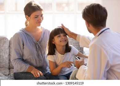 Caring male doctor stroking head of little girl patient sit on couch with mom, happy trusting child visiting talk to pediatrician showing good attitude relationships with kid at medical consultation