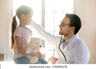 Caring Male Doctor Stroking Little Girl Patient Head At Meeting In Hospital Close Up Profile, Friendly Pediatrician Therapist Gp Calming Pretty Preschool Girl Hugging Fluffy Toy, Children Healthcare