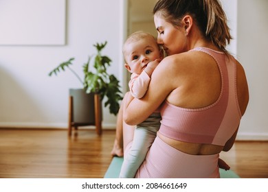 Caring Mom Working Out With Her Baby At Home. Loving Mom Holding Her Baby While Sitting On An Exercise Mat. New Mom Bonding With Her Baby During Her Post-natal Fitness Routine.