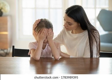 Caring mother calming and hugging crying upset little daughter, sitting at desk together, loving mum expressing support, comforting offended preschool girl, children psychologist concept